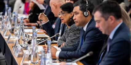 Delegates seated at a conference table with microphones and notepads, engaging in discussions.