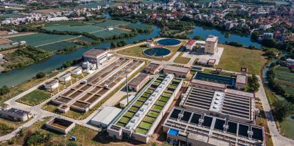 Aerial view of a wastewater treatment facility, surrounded by greenery and water bodies.