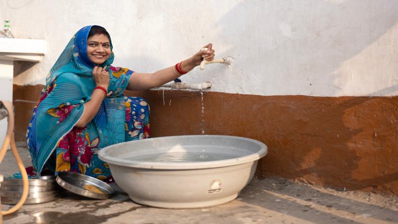 Indian woman washing utensils using a large pail.