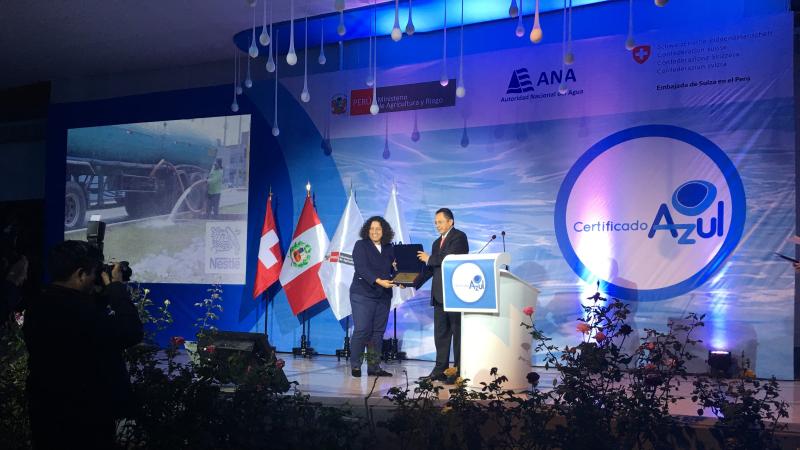 Two individuals on stage during an award ceremony, with the 'Certificado Azul' logo and Peruvian flags in the background.