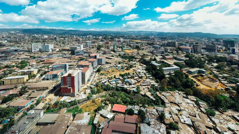 Aerial view of an urban cityscape with buildings, informal settlements, and greenery under a bright blue sky.