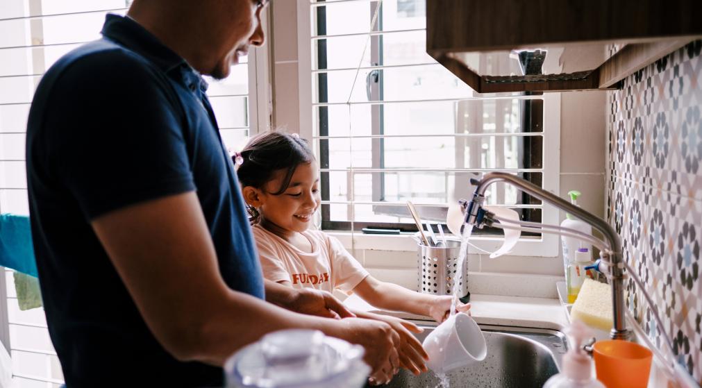 Parent and child washing dishes together at home.