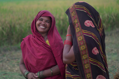 Two women interacting and smiling in a rural setting.